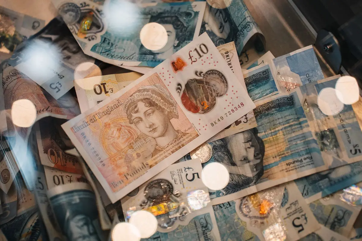 A loose pile of British five and ten pound banknotes lying on a surface, with soft out of focus lights across the frame