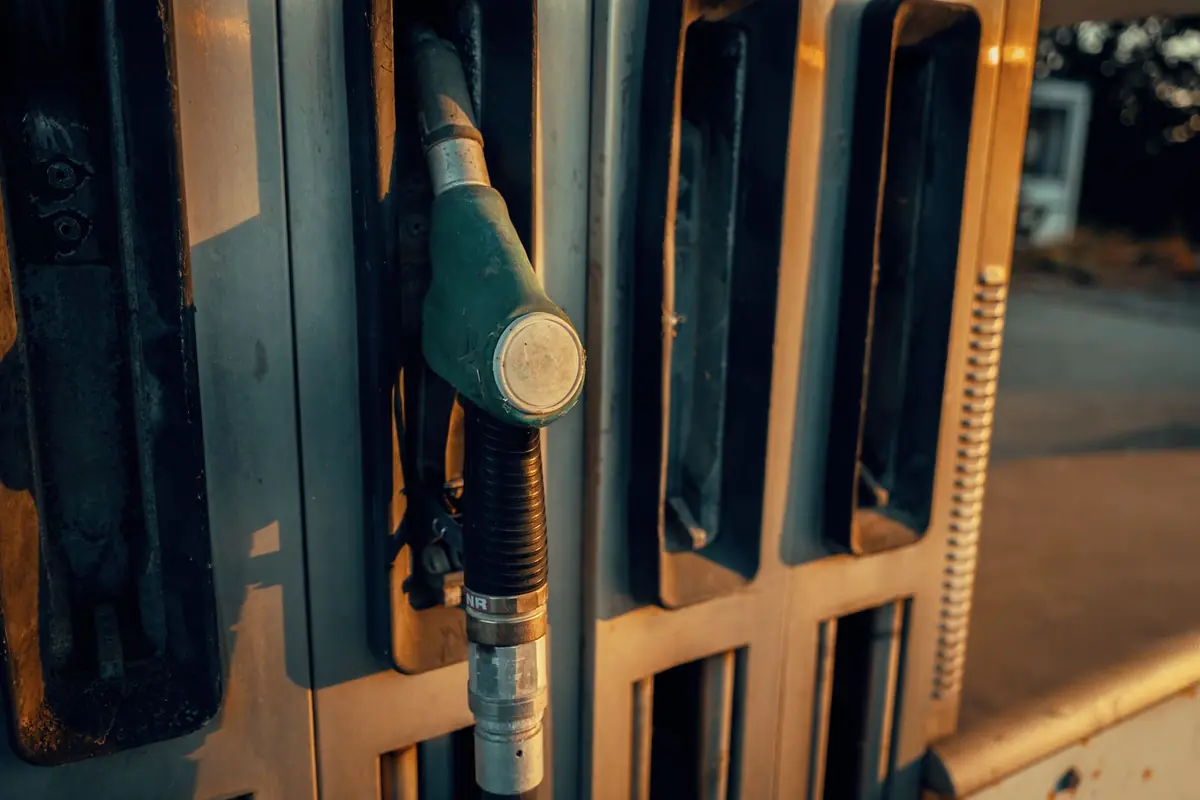 Close up of a green fuel nozzle resting in a worn metal petrol pump, lit by low evening sunlight