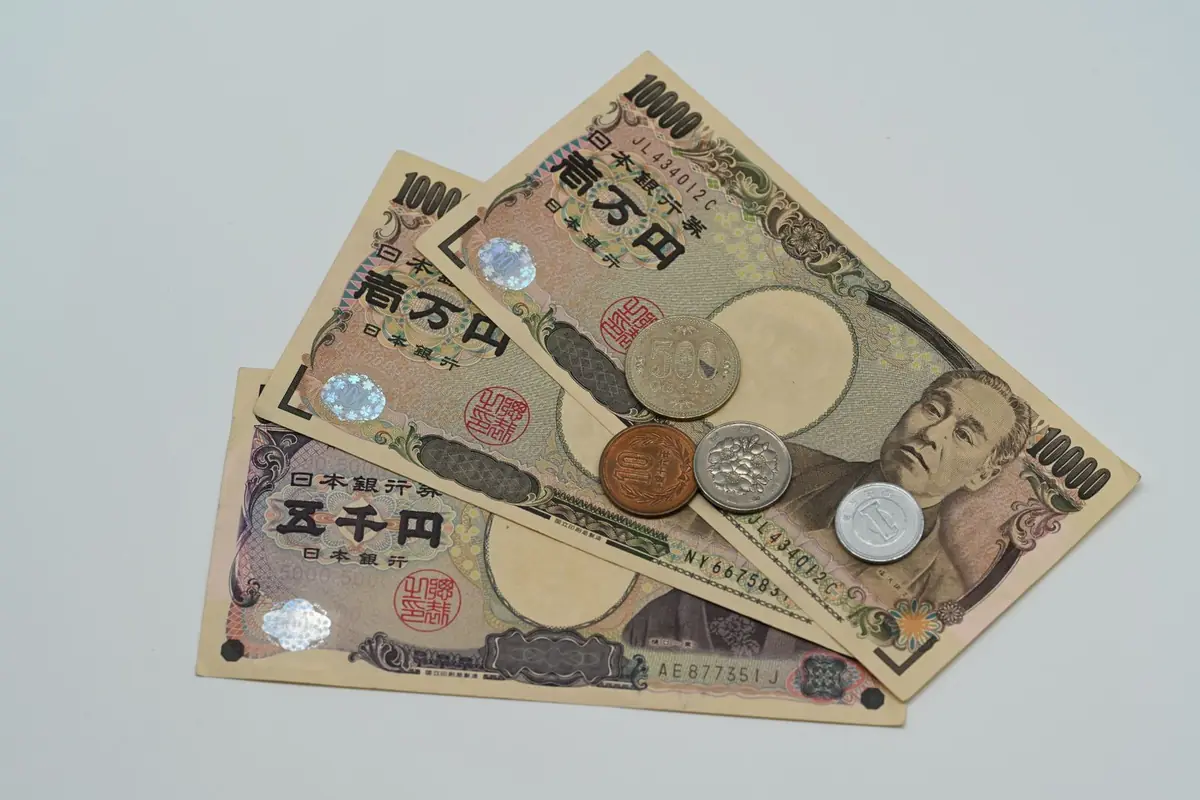 Japanese 10,000 and 5,000 yen banknotes fanned out on a pale surface with several yen coins on top